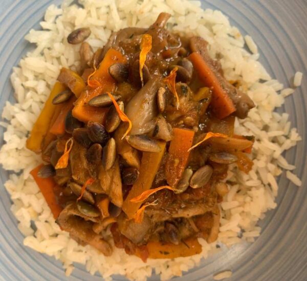 Plato azul con arroz blanco acompañado de un salteado de vegetales, hongos con curry de Tropical y semillas tostadas, decorado con pétalos de caléndula.