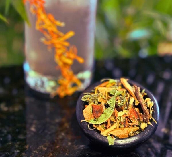 Infusión herbal con hojas y flores secas acompañada de bebida fría decorada con pétalos naranjas. Composición natural y refrescante.