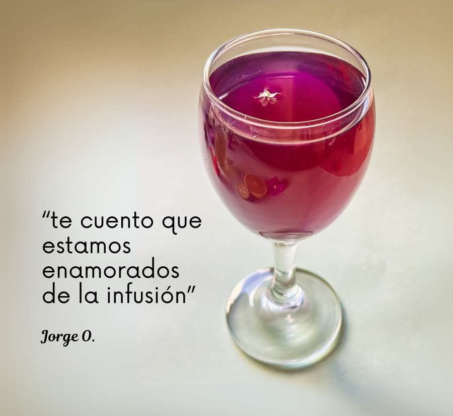 Vaso de cristal con infusión de color violeta intenso sobre fondo claro. Cita de cliente satisfecho resalta la experiencia sensorial del producto.