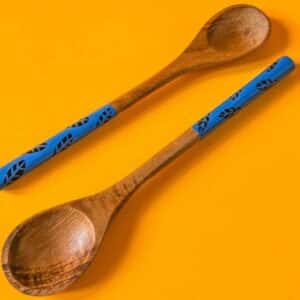 Par de cucharas de madera con mangos azules pintados a mano, sobre fondo naranja tropical.