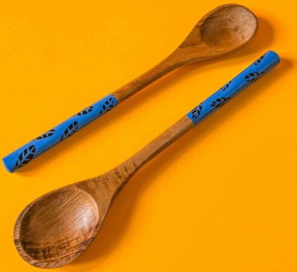Par de cucharas de madera con mangos azules pintados a mano, sobre fondo naranja tropical.