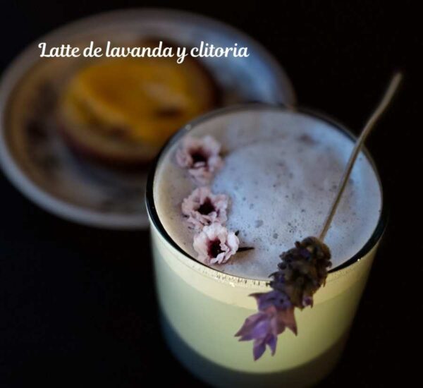 Taza de latte espumoso con lavanda y clitoria con flores comestibles sobre fondo oscuro. Bebida herbal con presentación elegante.